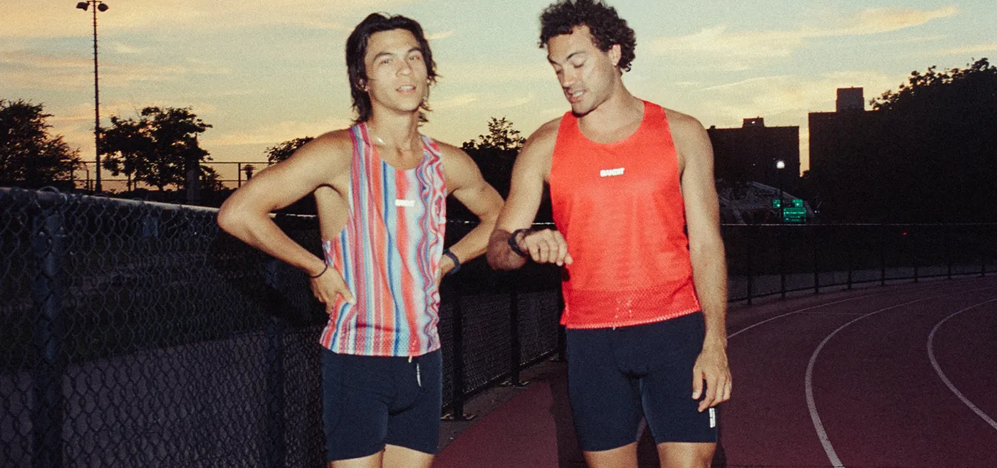 Two runners in Bandit singlets checking a watch on a track at sunset